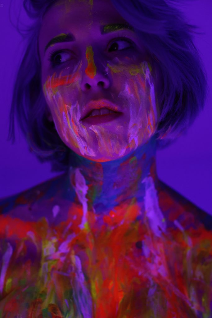 Self Portrait of Woman Under Black Light Covered in Neon Body Paint