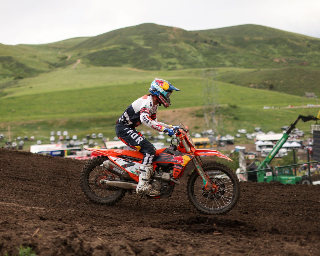 Professional Motocross rider on an KTM dirt bike racing on a muddy track.