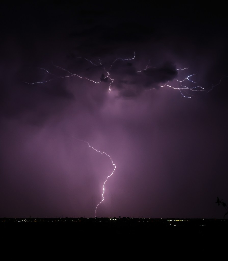 Lightning bolt striking during a thunderstorm over a distant cityscape.