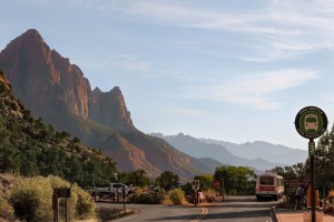 Zion National Park shuttle stop with scenic red rock mountains in the background under a clear blue sky.