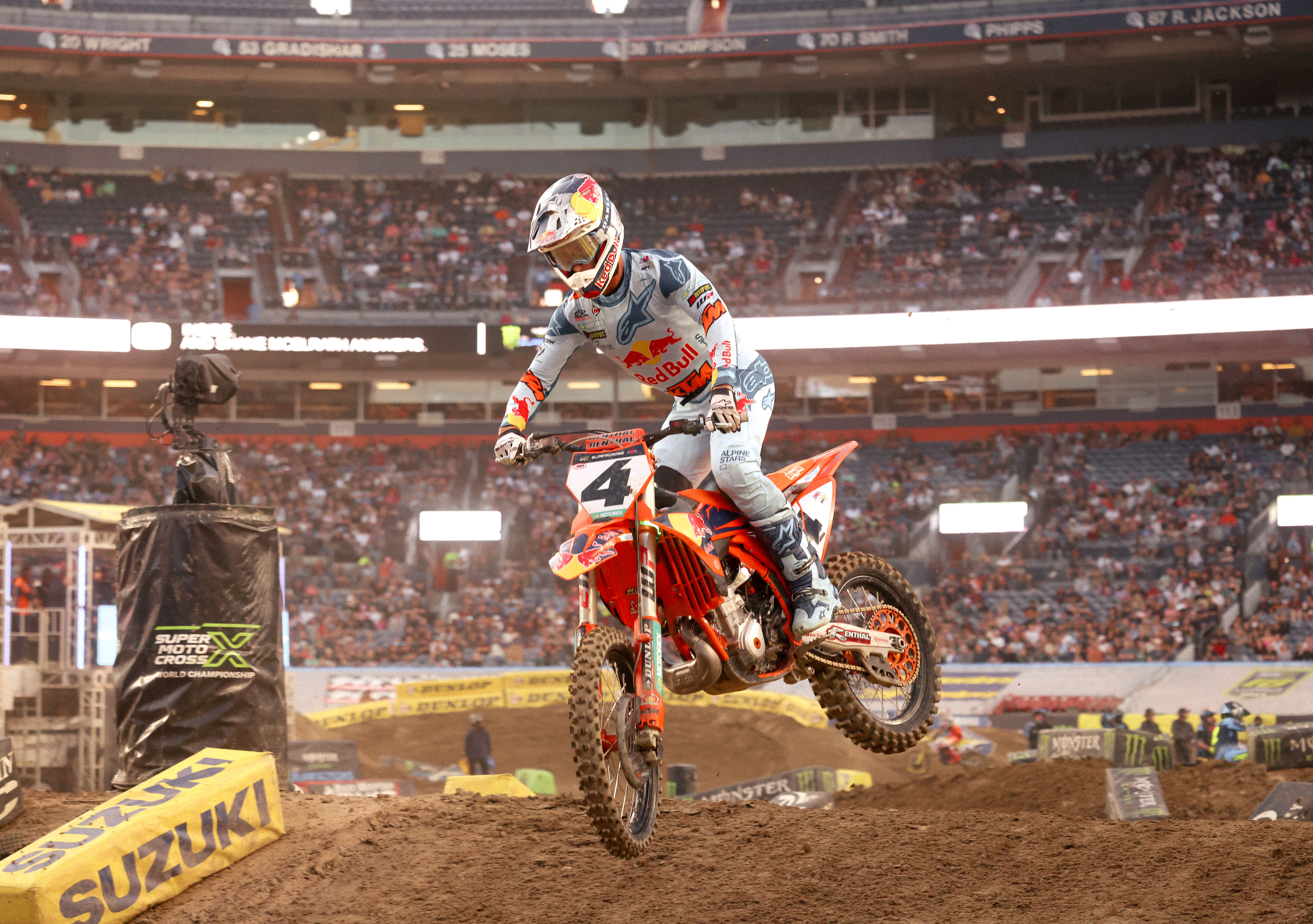 Chase Sexton number 4 jumping mid-air with stadium lights glowing behind him.