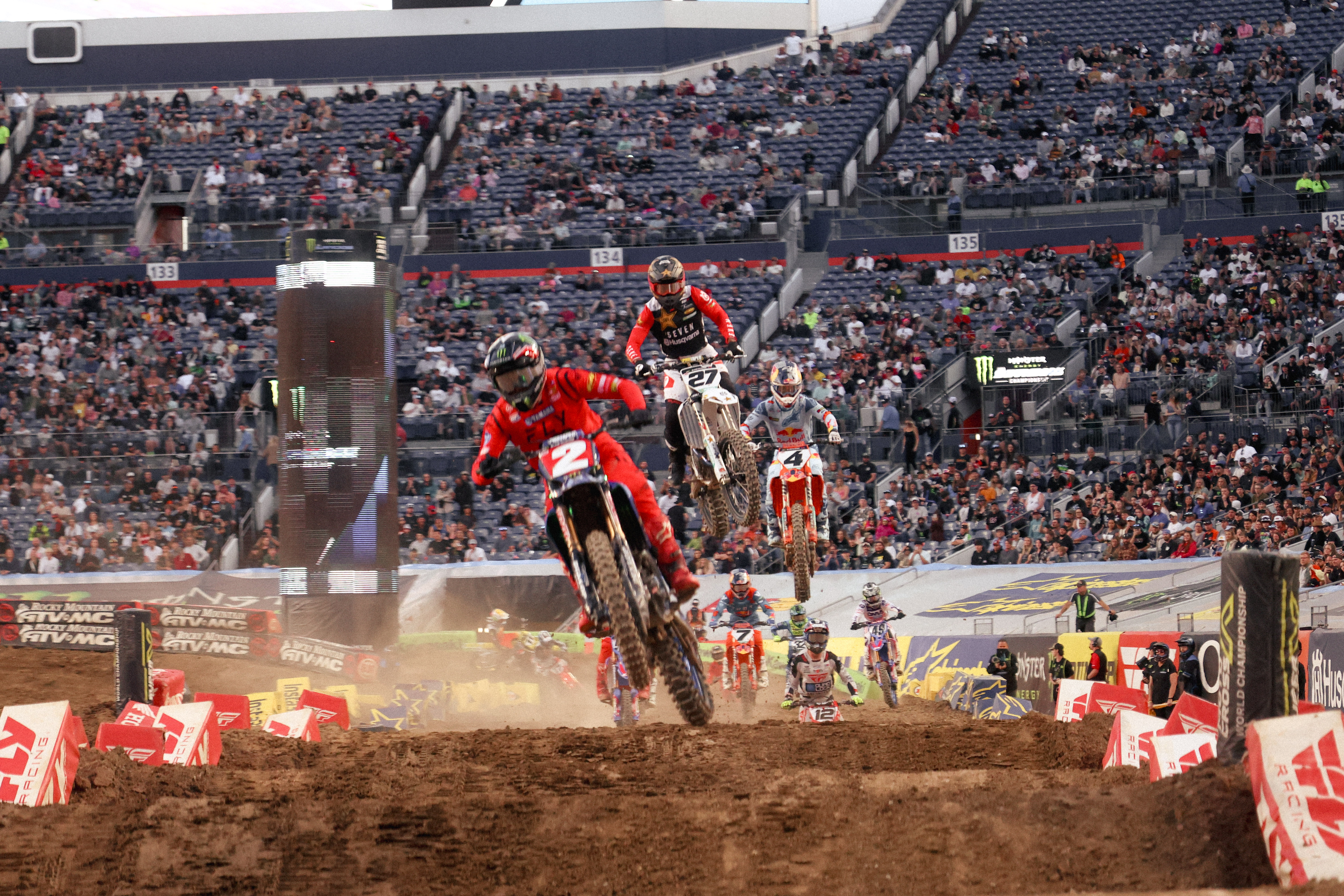 Multiple riders including Cooper Webb, Malcolm Stewart, and Chase Sexton battling in the first corner.