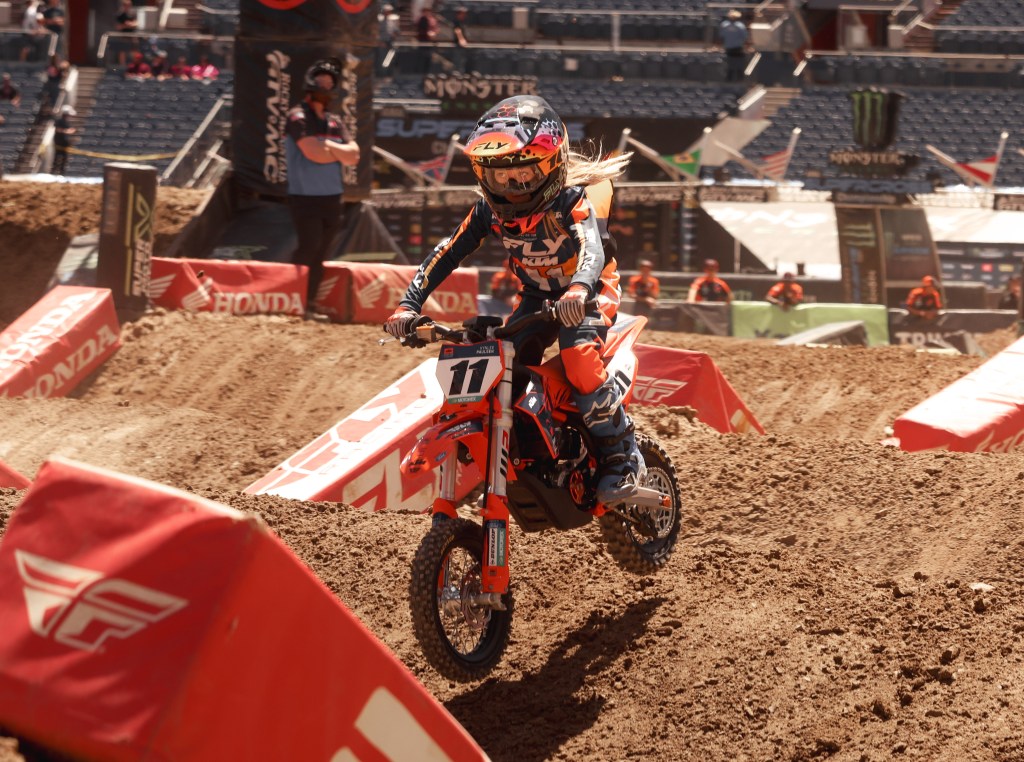 Kynlee Paulsen number 11, a KTM Junior rider, flying over a small jump lit by golden sun.