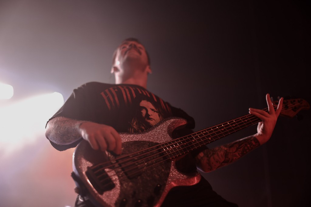 Ryne Olsen of The Home Team playing a sparkly bass guitar on stage under vibrant concert lights in Colorado, 2023.