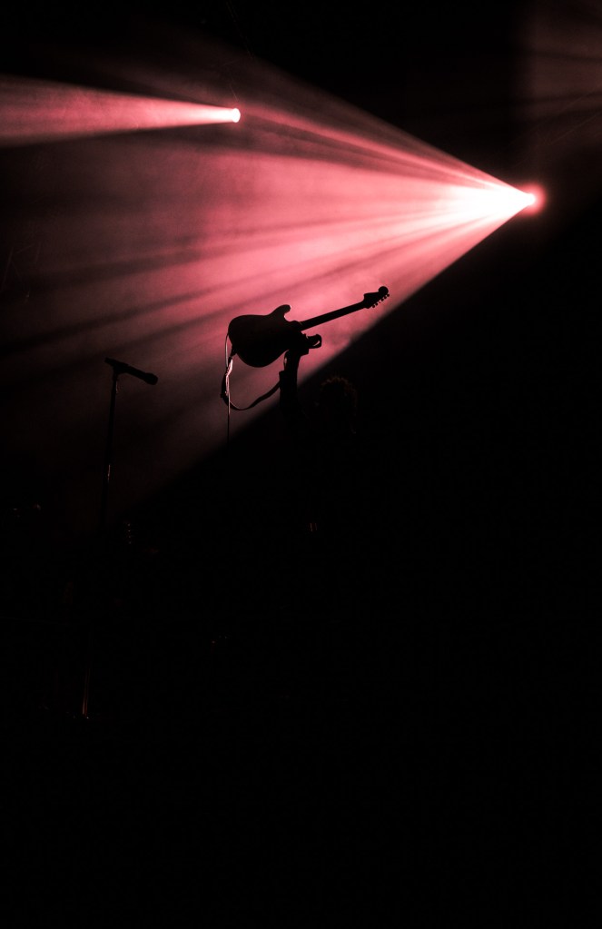 Christo Bowman from Bad Suns holding guitar up in front of stage light
