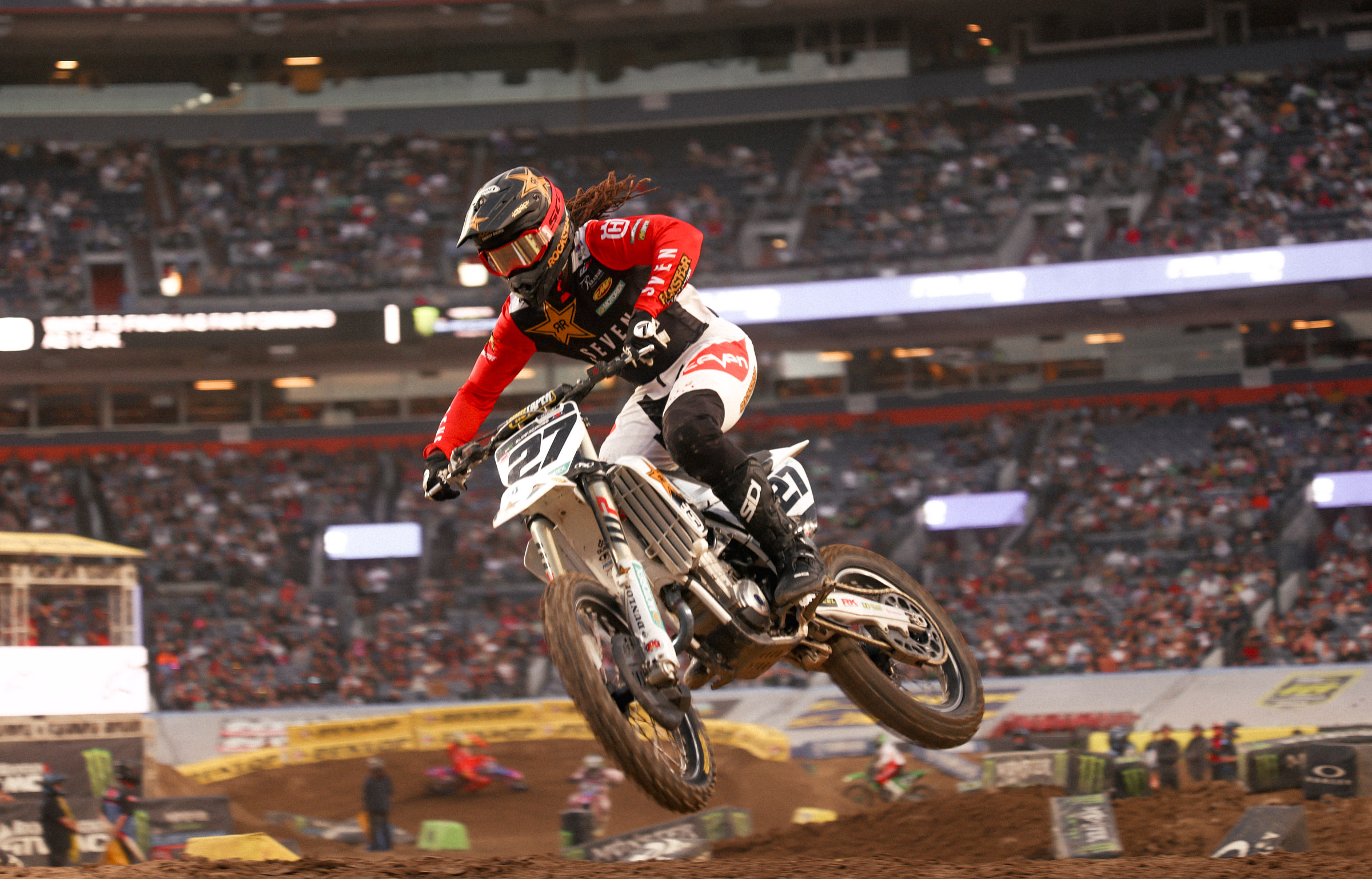 Malcolm Stewart number 27 riding with his dreadlocks flowing, Rockstar logo colors highlighted.